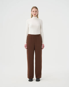 Chandail Turtleneck blanc ivoire pour femme et pantalon ample brun à taille élastique. 